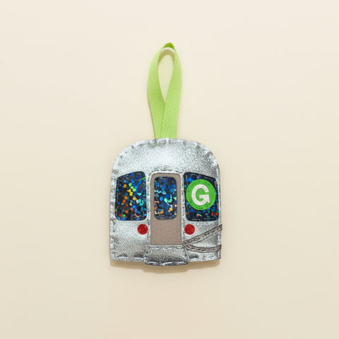 Decorative ornament shaped like a train car with a green 'G' on a wooden surface