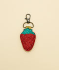 Strawberry-shaped keychain with glittery red body and green top on a wooden surface