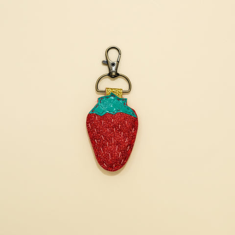 Strawberry-shaped keychain with glittery red body and green top on a wooden surface