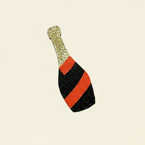 Decorative bottle-shaped object with gold top, red middle, and black bottom on a wooden surface