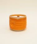 Orange candle in a textured holder.