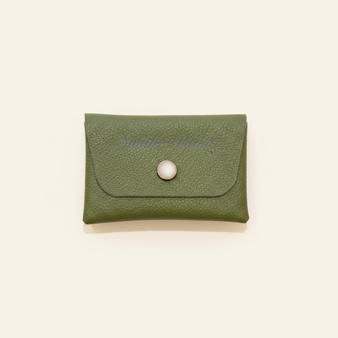 Green leather wallet with a button on a wooden surface