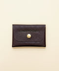 Burgundy leather cardholder with a gold button on a wooden surface