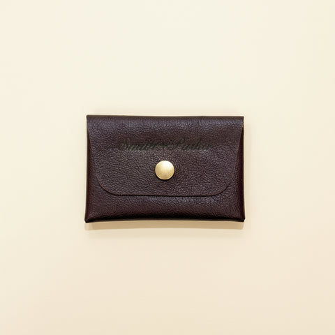 Burgundy leather cardholder with a gold button on a wooden surface