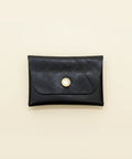 Black leather cardholder with a pearl button on a wooden surface