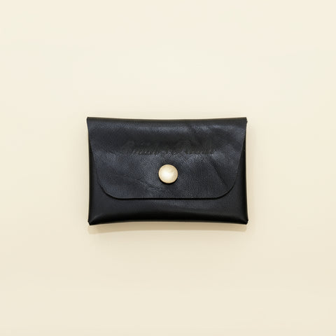 Black leather cardholder with a pearl button on a wooden surface