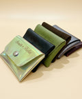 Four leather wallets in different colors on a wooden surface with a clear plastic card holder.