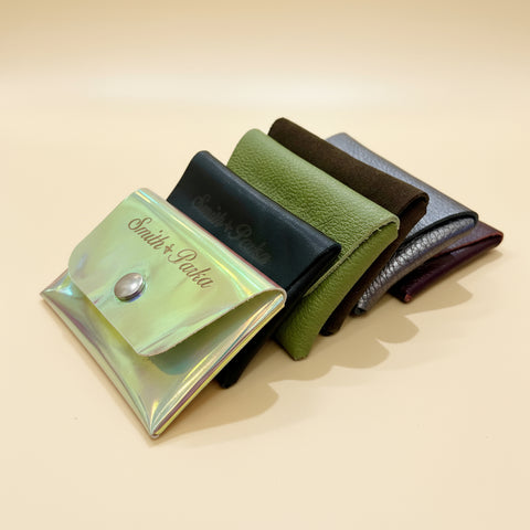 Four leather wallets in different colors on a wooden surface with a clear plastic card holder.