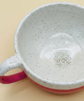 Speckled ceramic mug with pink handle and base on a wooden surface