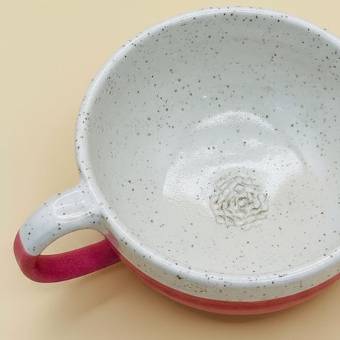 Speckled ceramic mug with pink handle and base on a wooden surface