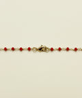 Gold bracelet with red beads on a wooden surface