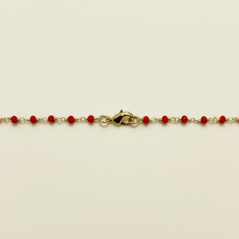 Gold bracelet with red beads on a wooden surface