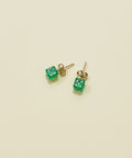 Green dice-shaped stud earrings on a wooden surface
