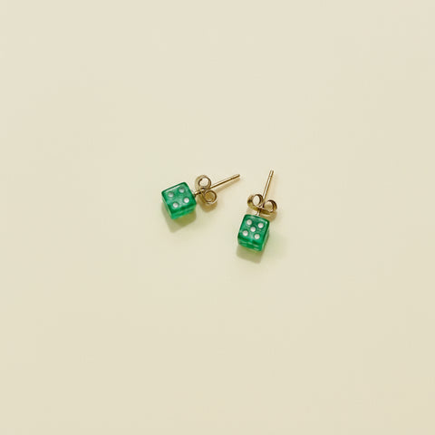 Green dice-shaped stud earrings on a wooden surface