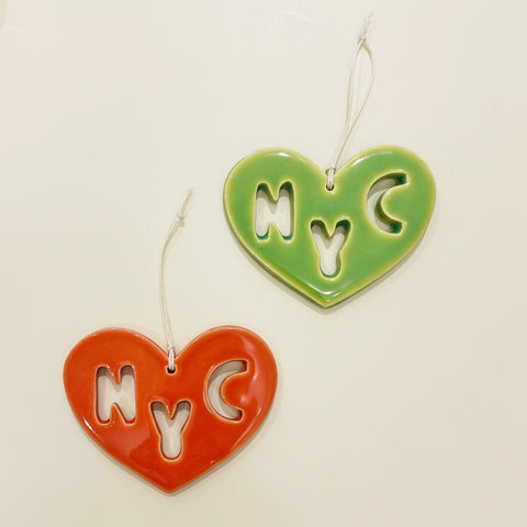 Two heart-shaped 'NYC' cutout charms on a wooden surface.