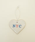 Heart-shaped ceramic tag with 'NYC' on a wooden surface