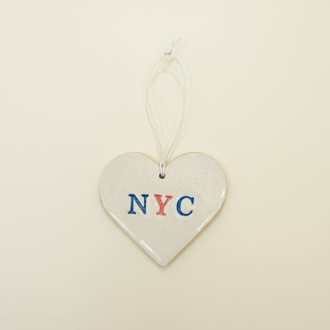 Heart-shaped ceramic tag with 'NYC' on a wooden surface