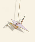 Decorative paper crane hanging on a wooden surface with a blurred background of shelves.