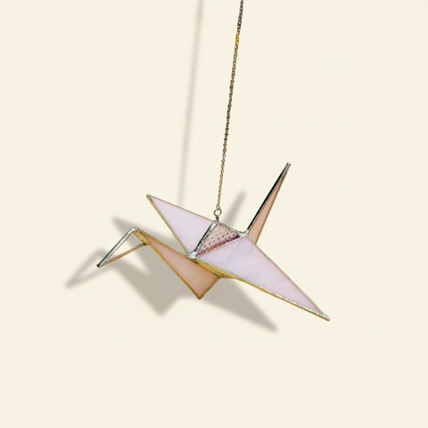 Decorative paper crane hanging on a wooden surface with a blurred background of shelves.