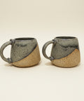 Two ceramic mugs with handles on a wooden surface, blurred indoor background