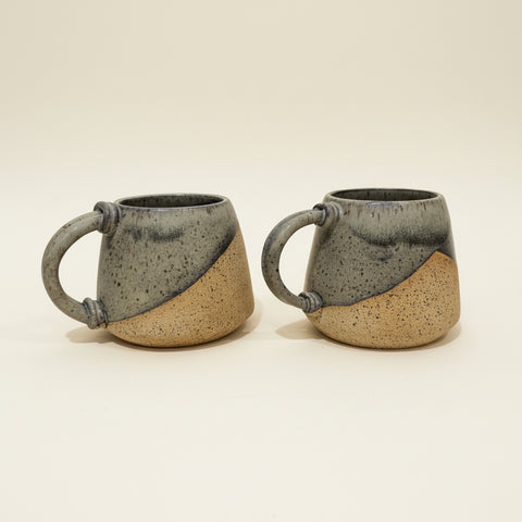 Two ceramic mugs with handles on a wooden surface, blurred indoor background
