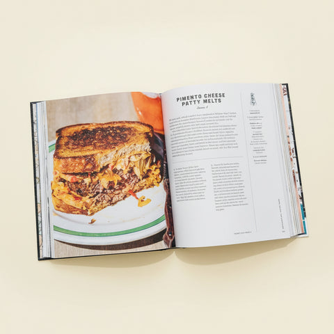 Open cookbook on a wooden table with a laptop and ingredients nearby