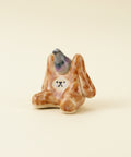Small ceramic figurine of a rabbit with a pigeon on its back on a wooden surface.
