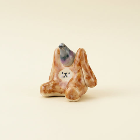Small ceramic figurine of a rabbit with a pigeon on its back on a wooden surface.