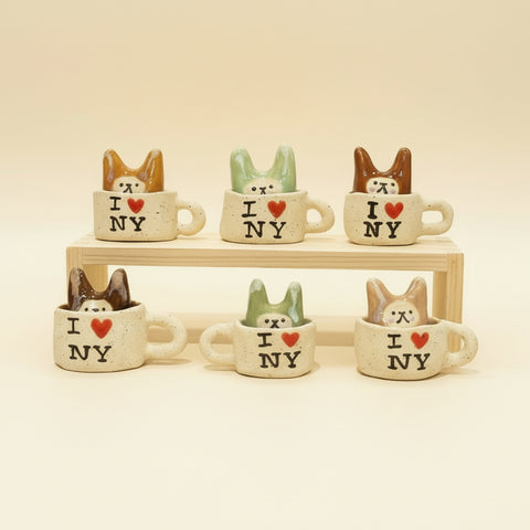 Set of small ceramic mugs with cat designs and 'I ❤️ NY' text on a wooden surface.