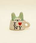 Ceramic mug with 'I ❤️ NY' text and a small figurine inside on a wooden surface.