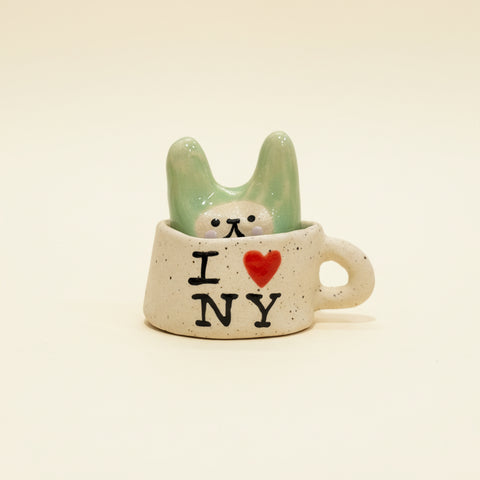 Ceramic mug with 'I ❤️ NY' text and a small figurine inside on a wooden surface.