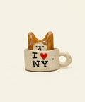 Small ceramic cup with a cat design and 'I ❤️ NY' text on a wooden surface.