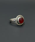Silver ring with a red stone on a wooden surface