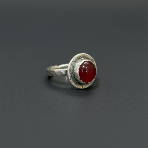 Silver ring with a red stone on a wooden surface