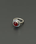 Silver ring with a red stone on a wooden surface