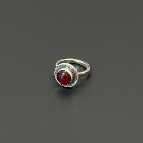 Silver ring with a red stone on a wooden surface