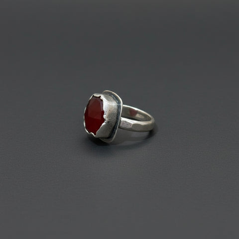 Silver ring with a red stone on a wooden surface