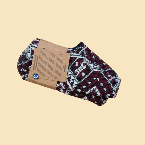 Pair of patterned socks with a cardboard tag on a wooden surface, with a person wearing blue jeans in the foreground.