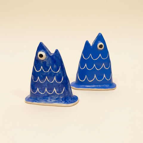 Two blue ceramic fish figurines on a wooden surface with a laptop in the background.