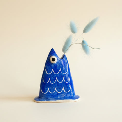 Blue ceramic fish ornament on a wooden surface with a blurred office background