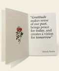 Open book with a floral illustration and motivational quote on a wooden surface