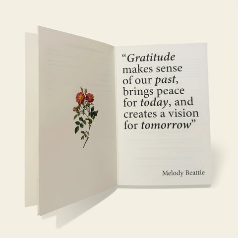 Open book with a floral illustration and motivational quote on a wooden surface