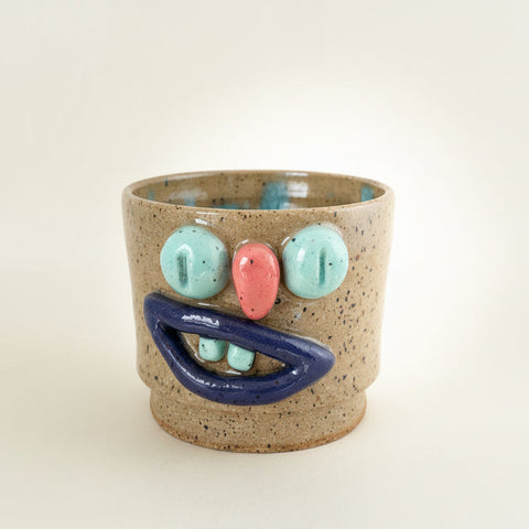 Ceramic cup with colorful face design on a beige background