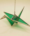 Green stained glass crane ornament on a wooden surface with a blurred indoor background