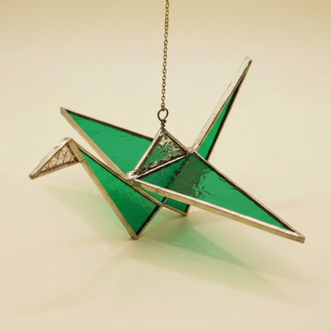 Green stained glass crane ornament on a wooden surface with a blurred indoor background