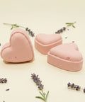 Three pink heart-shaped objects on a wooden surface with a laptop in the background.