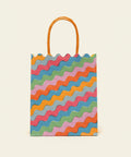 Colorful wavy-patterned gift bag with orange handle on a wooden surface.