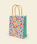 Colorful smiley face gift bag with orange handles on a wooden surface.