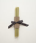 Two green candles wrapped together with a brown paper band on a wooden surface.