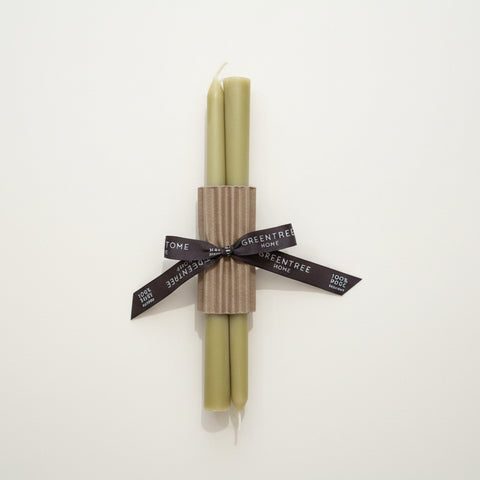 Two green candles wrapped together with a brown paper band on a wooden surface.